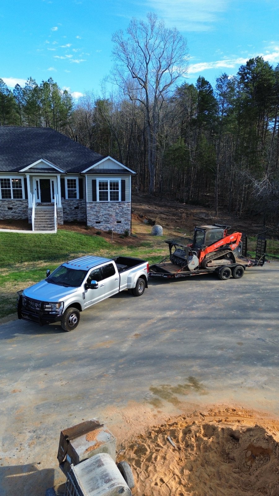 Aerial view of truck, trailer, and track loader mulcher staged at a residential job site